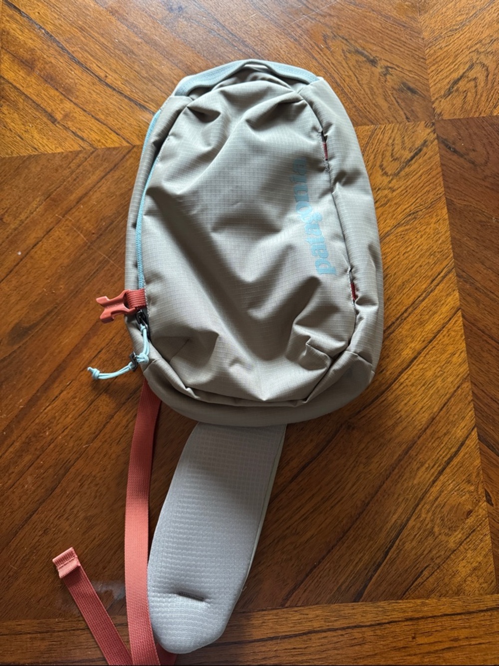 Patagonia beige  8L sling pack with pale blue logo and coral accents